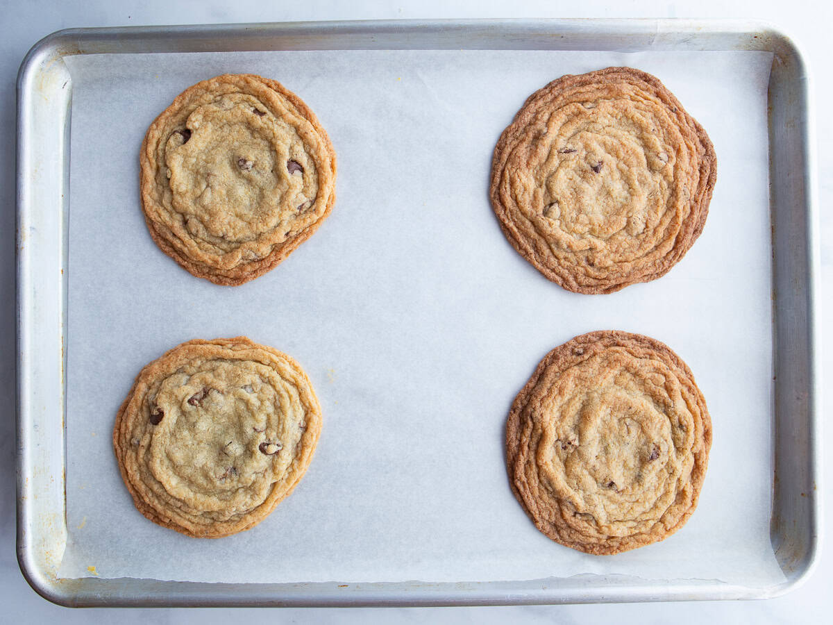 Four gluten-free chocolate chip cookies on a baking sheet.