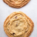 Two large gluten-free chocolate chip cookies on a pan. The edges of the cookies are wrinkled.