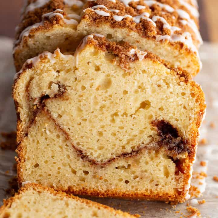 Gluten-free cinnamon swirl bread, topped with cinnamon sugar and a vanilla glaze, sits on a cutting board. Two slices are cut from the bread to show the layer of brown sugar and cinnamon in the center.