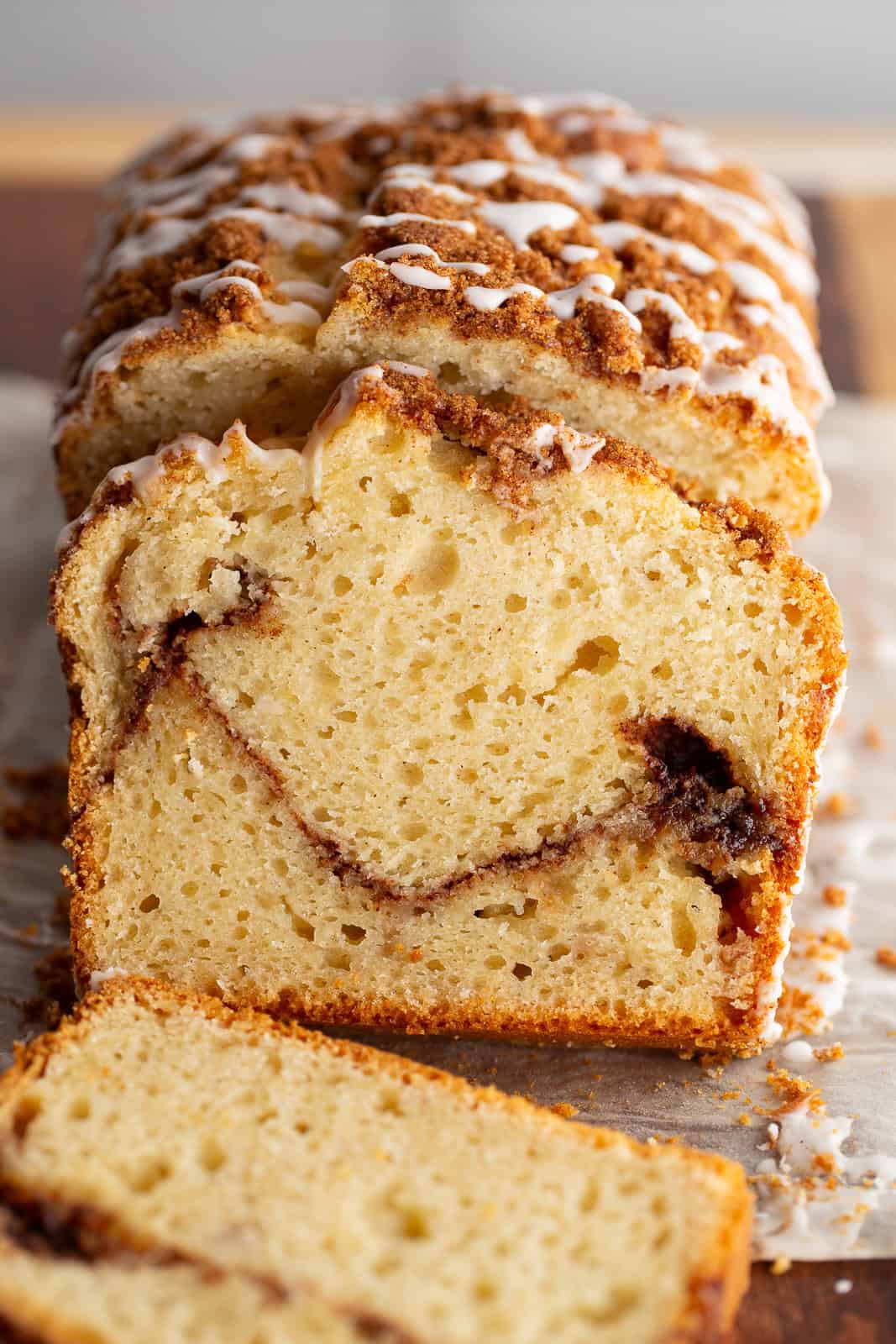 Gluten-free cinnamon swirl bread, topped with cinnamon sugar and a vanilla glaze, sits on a cutting board. Two slices are cut from the bread to show the layer of brown sugar and cinnamon in the center.